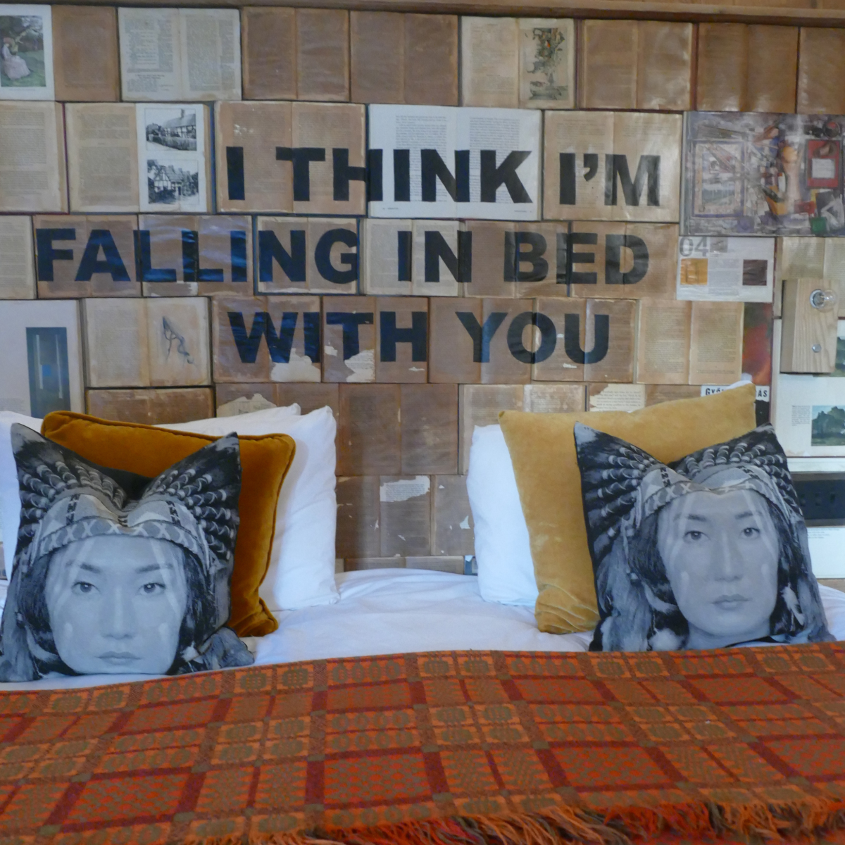 Bedroom at The Bell, Ticehurst, with bold wall text reading “I think I’m falling in bed with you” above patterned cushions and bed.